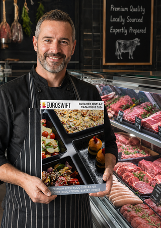 Butcher holding the Euroswift Butcher Display Catalogue 2026 in a premium butcher shop